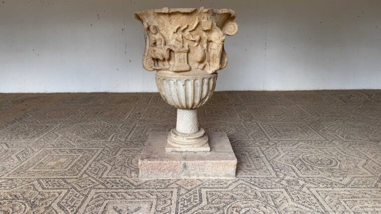 Relief-carved marble basin or urn on a pedestal, with a fluted lower body and figural decoration above a mosaic floor.
