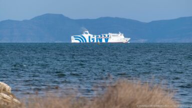 White-and-blue passenger ferry crossing the Gulf of Tunis with hazy mountain ridges in the background.