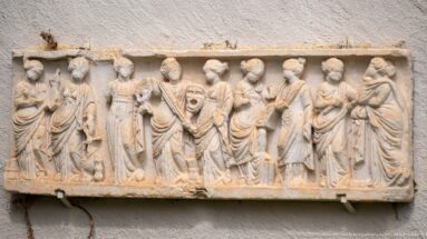 Rectangular pale stone relief carved with a procession of standing and gesturing draped figures.