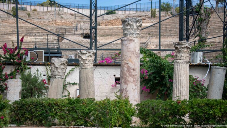 Weathered ancient column shafts and Corinthian-style capitals displayed before the stone seating of the Roman Theatre.
