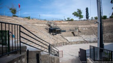 Curving tiers of stone seating inside the Roman Theatre of Carthage with modern railings and stage equipment.