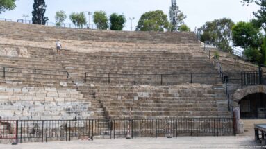 Close view of stepped stone theatre seating with weathered and restored masonry, railings, and a visitor for scale.