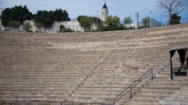 Upper stone seating of the Roman Theatre of Carthage with repaired masonry, railings, trees, and distant mosque minaret.