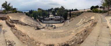 Wide elevated overview of the Roman Theatre of Carthage showing curving seating, central stage area, and surrounding trees.