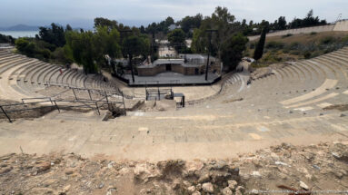 Centered high-angle view of the Roman Theatre of Carthage with curving stone seating around the stage.