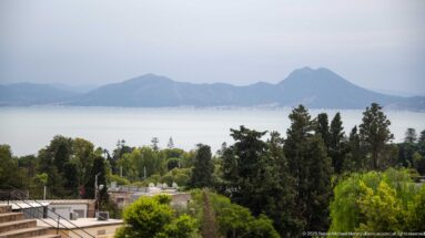 Elevated view from Carthage across trees and rooftops to the Gulf of Tunis and hazy mountain ridges.
