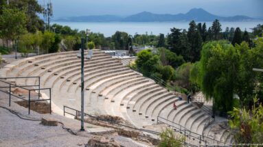 Curving upper seating of the Roman Theatre of Carthage overlooking trees, the Gulf of Tunis, and distant mountains.