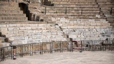 Close view of weathered and restored stone theatre seating with an access opening and black protective railings.