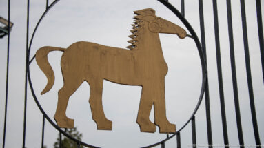 Golden stylized horse cutout inside a circular black metal frame against a pale sky.