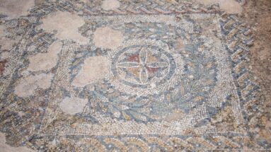 Circular Roman mosaic medallion with four-petal center, interlaced geometric bands, and worn tesserae.