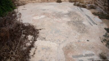 Worn Roman mosaic floor with fragmentary dark geometric bands and faint colored tesserae.