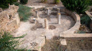 Semicircular Roman masonry enclosure with short columns arranged around a paved central area.