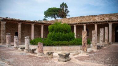Reconstructed Roman villa courtyard with marble columns, central greenery, paved floor, and covered portico.
