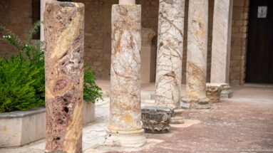 Close view of reddish and pale veined marble columns with bases in a reconstructed Roman villa peristyle.