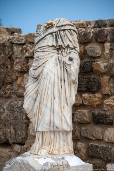 Fragmentary white marble statue with deeply carved layered drapery, missing its head and upper body.