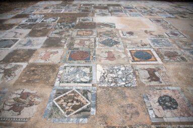 Large floor display of many Roman mosaic and colored-stone panels with geometric, floral, and figural motifs.