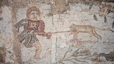 Roman mosaic of a tunic-clad figure holding a long pole toward a spotted animal amid vegetation.