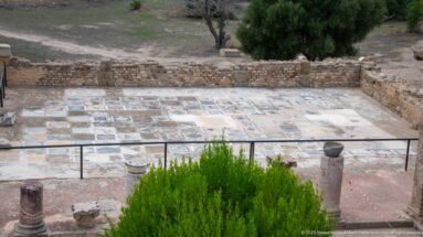 Elevated view of a large Roman villa pavement area filled with mosaic and colored-stone panels behind protective railings.