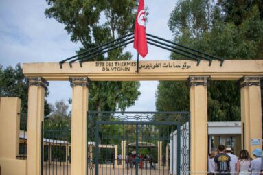 Bilingual entrance gateway for the Baths of Antoninus with French and Arabic site name beneath a Tunisian flag.