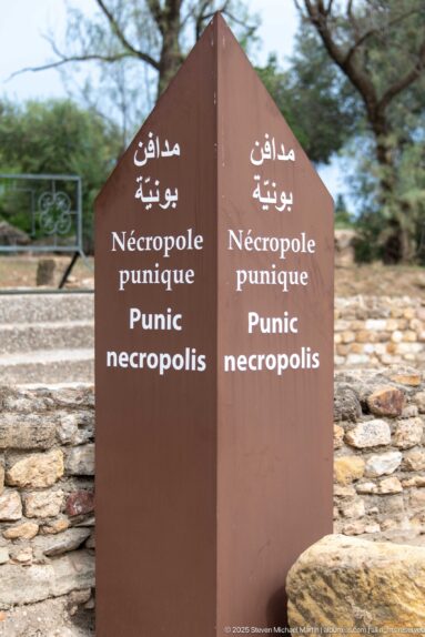Brown multilingual directional sign reading Punic necropolis in Arabic, French, and English.