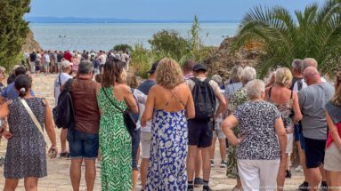 Tour group walking downhill through the Carthage archaeological park toward coastal ruins and the Mediterranean.