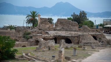 Ruins of the Baths of Antoninus with the Gulf of Tunis, palms, and twin-peaked Bou Kornine in the distance.