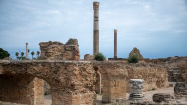 Two tall columns above vaulted ruins of the Baths of Antoninus with a carved capital fragment in the foreground.