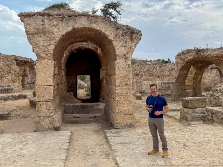 Large rounded stone arch leading into a dark passage in the Baths of Antoninus, with a visitor for scale.