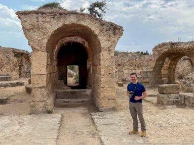 Large rounded stone arch leading into a dark passage in the Baths of Antoninus, with a visitor for scale.