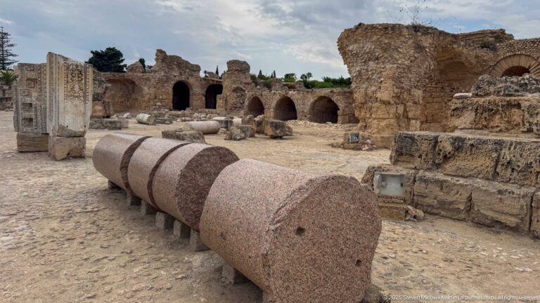 Massive pink granite column shaft displayed horizontally among the ruins of the Baths of Antoninus.