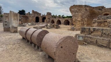 Massive pink granite column shaft displayed horizontally among the ruins of the Baths of Antoninus.