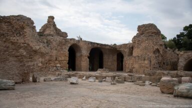 Ancient stone chambers at Carthage with tall arched openings, rough masonry walls, and scattered architectural fragments.