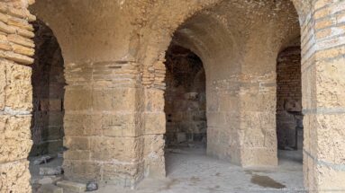 Interior of ancient vaulted masonry with thick piers, rounded arches, and visible brick courses.