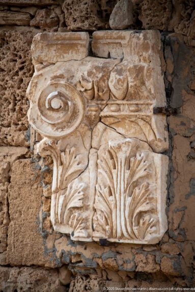 Pale carved stone panel with acanthus leaves, scrolling stems, and circular classical ornament.