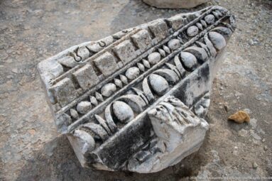 Broken carved stone cornice fragment with egg-and-dart, dentils, bead molding, and leaf ornament.