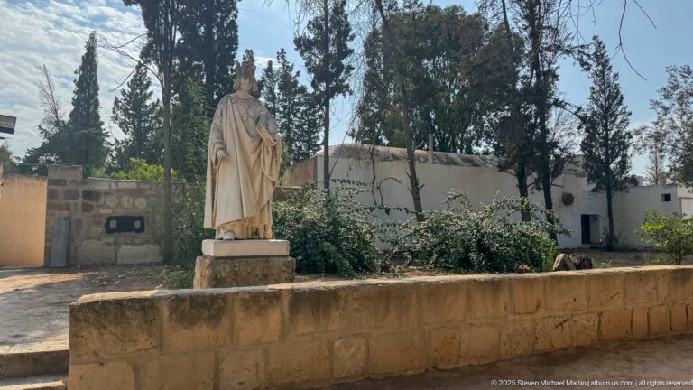 Stone statue of a robed cleric holding a book or document on a pedestal among trees at Byrsa Hill.