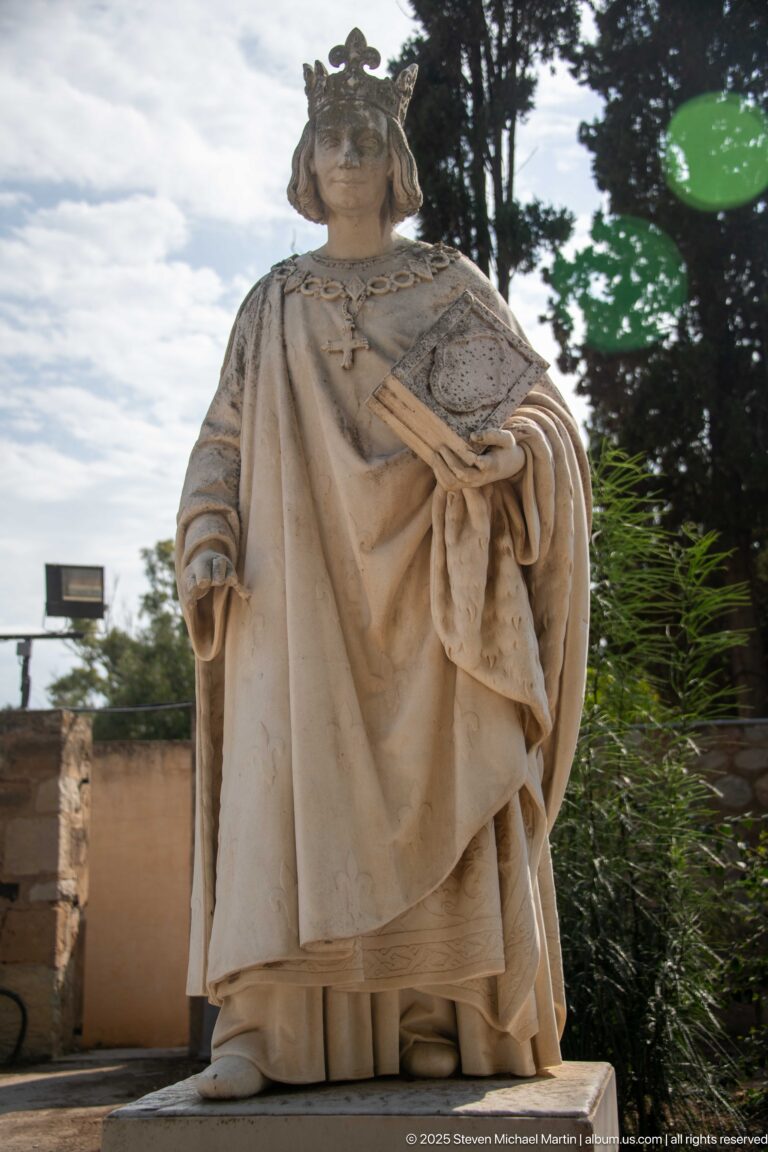 Low-angle view of a stone cleric statue in ceremonial robes holding a decorated book or plaque.