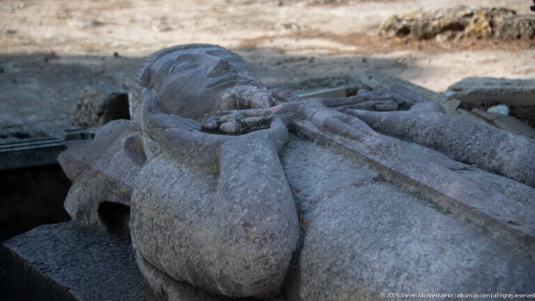 Close detail of sculpted hands resting over the chest of a stone recumbent effigy in heavy robes.
