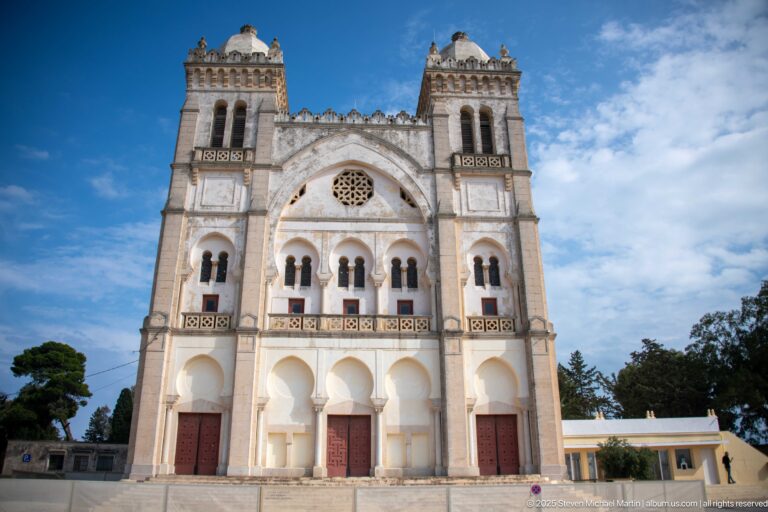 Centered view of Carthage L’Acropolium’s twin-towered façade with triple arches, rose-window tracery, and patterned stonework.