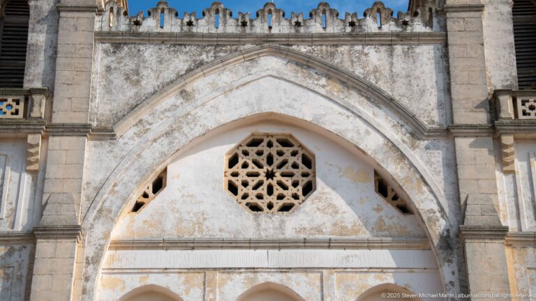 Pointed masonry arch framing an octagonal geometric tracery window on the weathered façade of Carthage L’Acropolium.