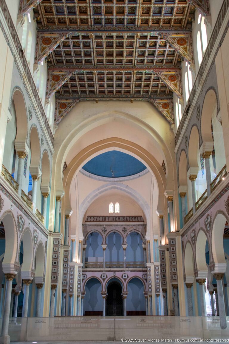 Wide nave interior of Carthage L’Acropolium with side galleries, painted arcades, a large transverse arch, and decorated ceiling.