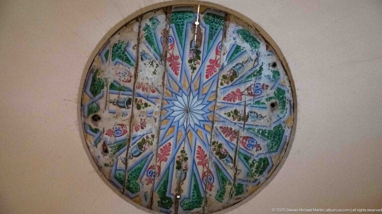 Circular stained-glass window with a starburst center and radiating blue, green, red, and pale ornamental panels.