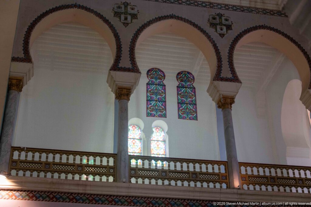 Triple-arched upper gallery with slender columns, gilded capitals, patterned borders, and paired stained-glass windows.