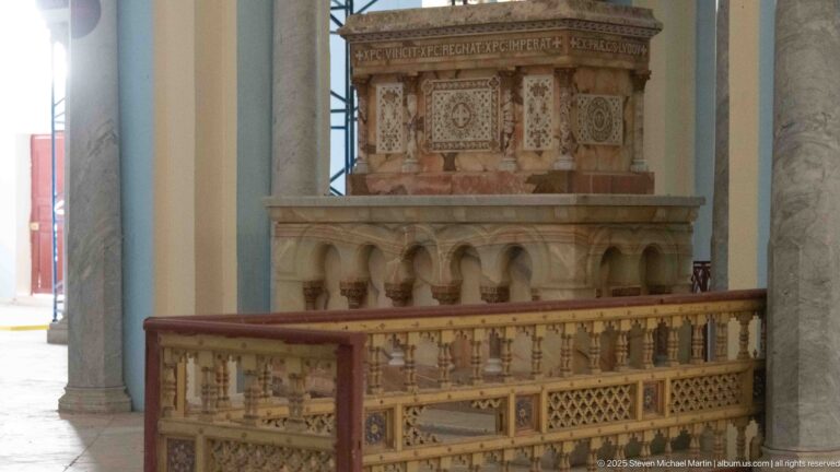 Ornate raised pulpit-like structure with carved balustrade, small arches, and painted geometric ornament inside the Acropolium.