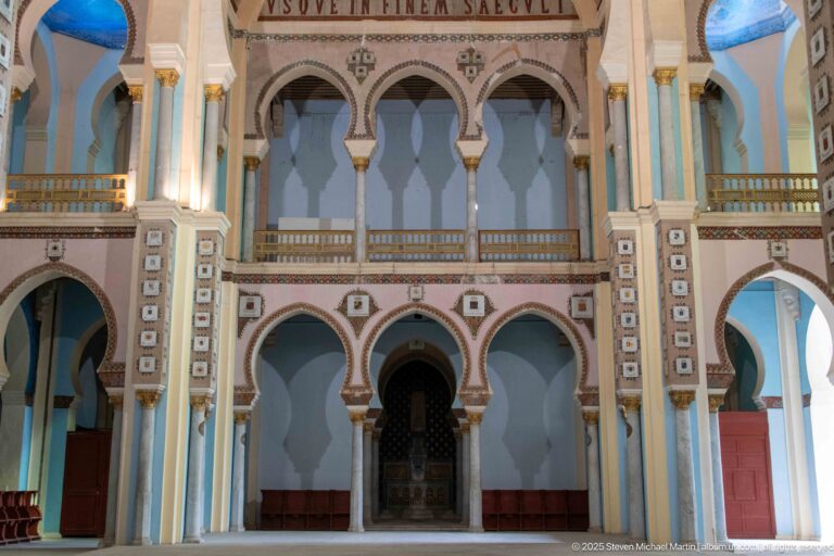 Symmetrical two-level interior arcade with a central dark doorway, stacked arches, slender columns, and patterned wall panels.