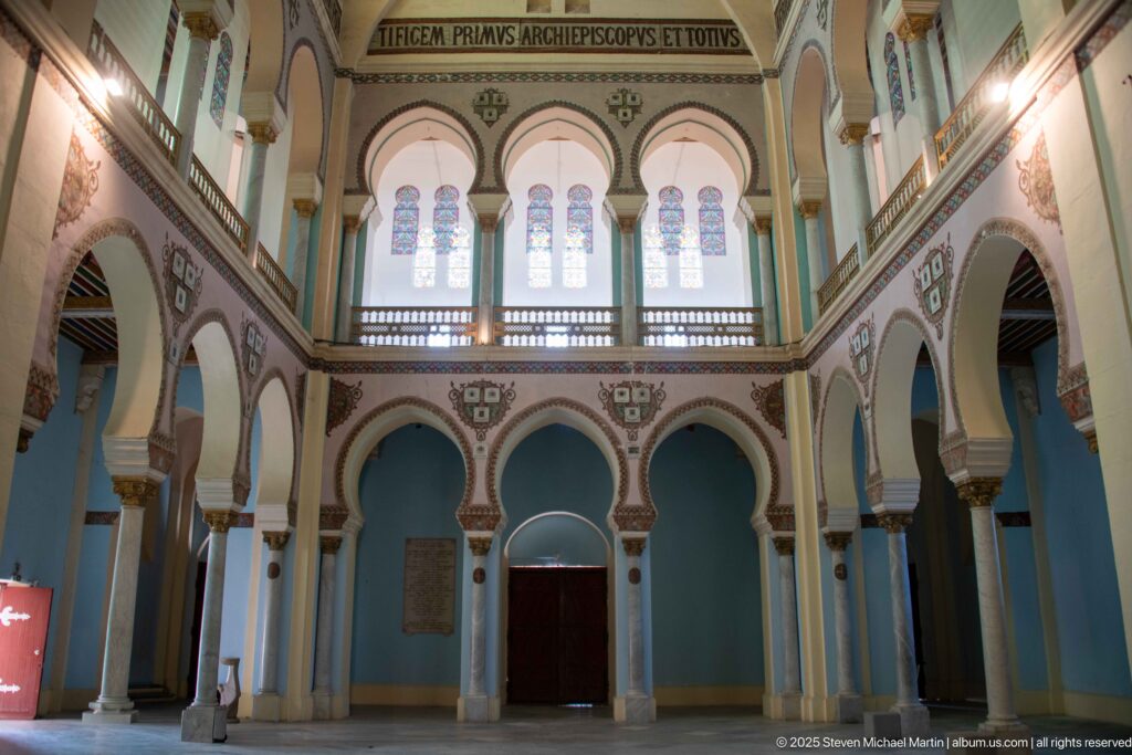Centered interior elevation with three pairs of stained-glass windows above a gallery, triple arcade, and central doorway.
