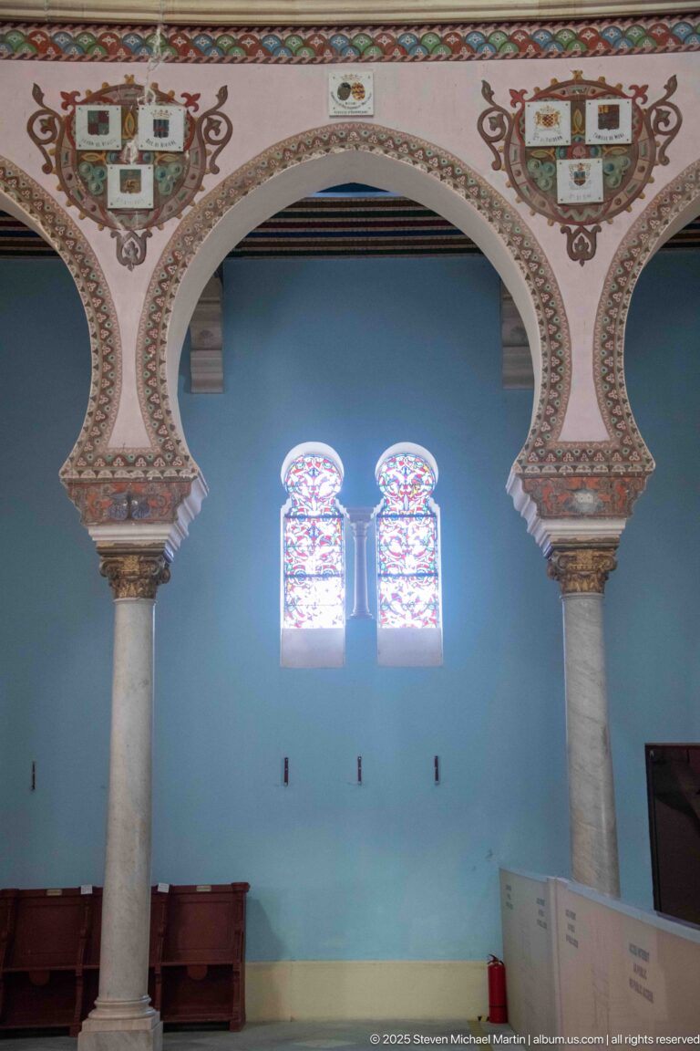 Large decorated arch framing two stained-glass windows on a blue wall, with a painted heraldic emblem above.