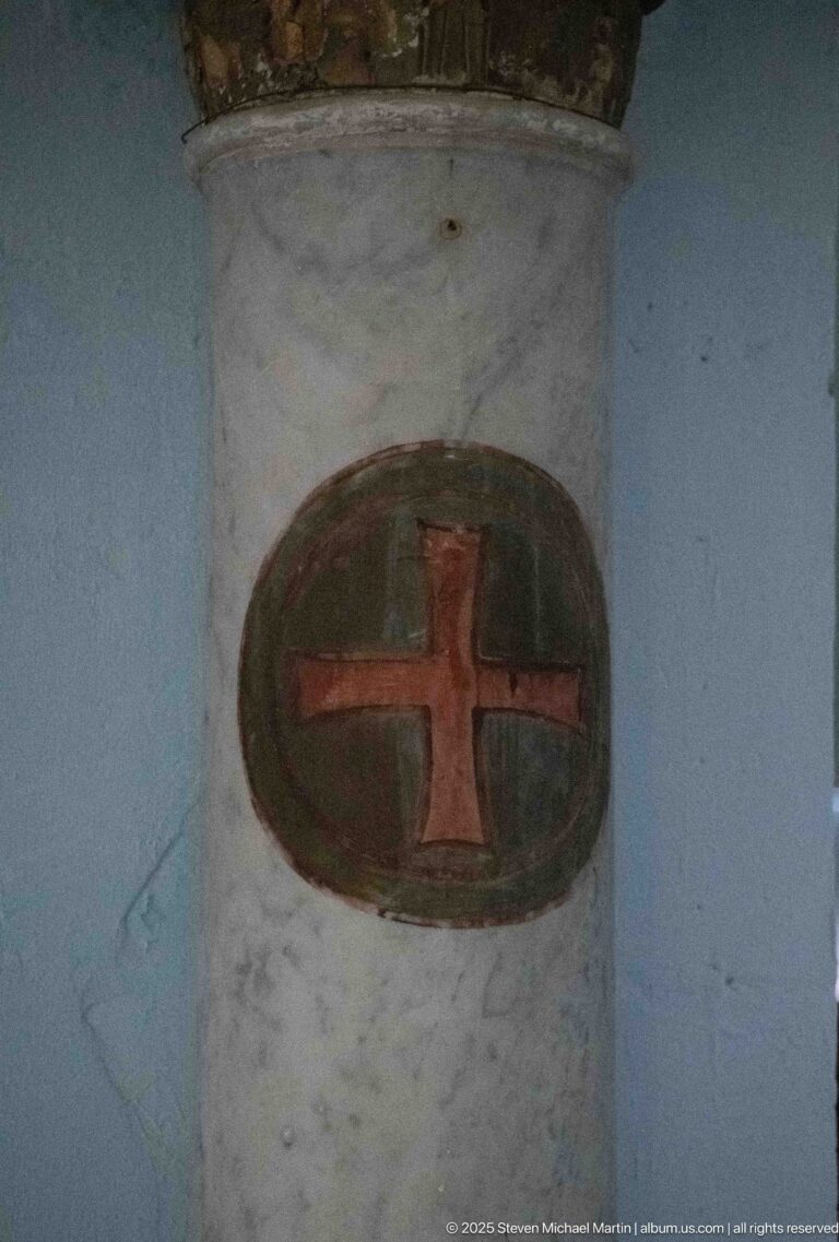 Red equal-armed cross painted inside a dark oval medallion on a pale interior column.