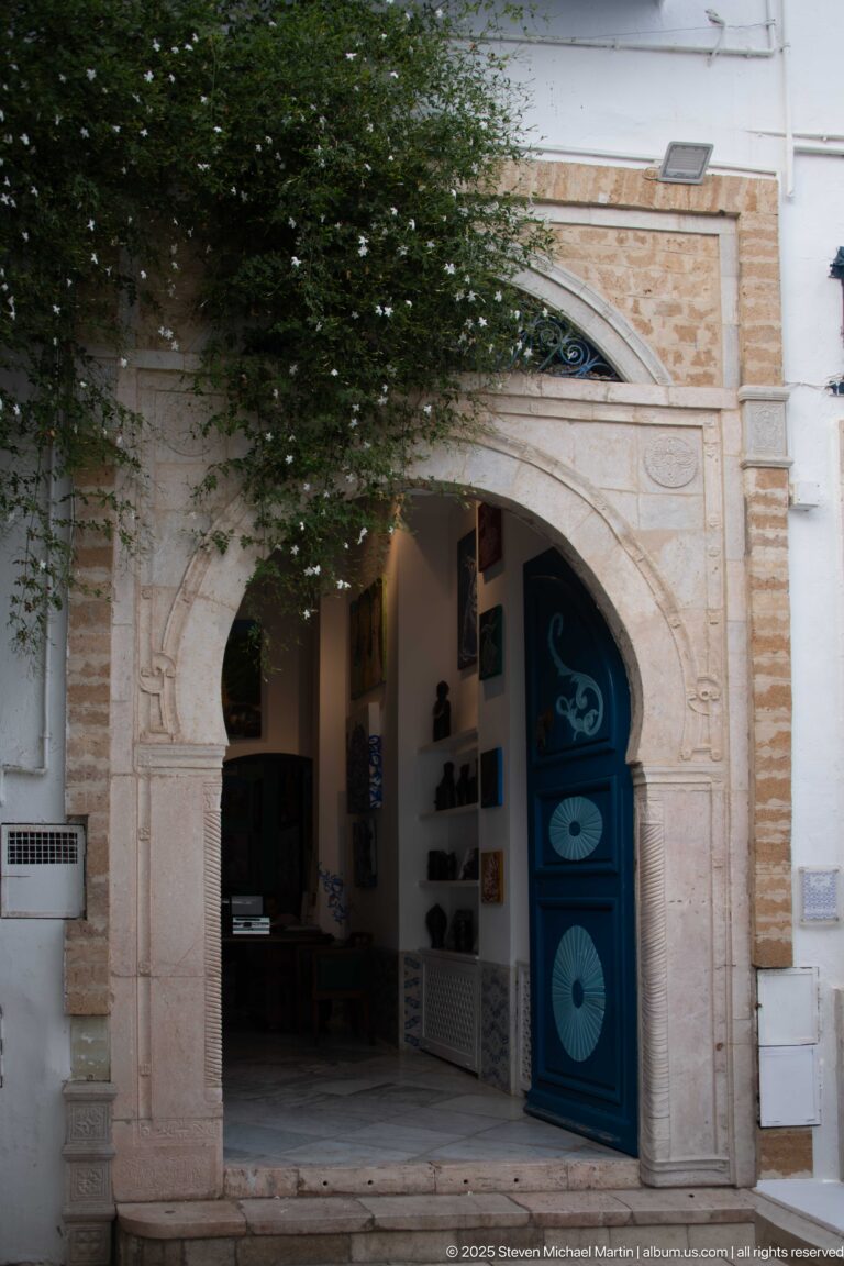 Carved pale-stone arch surrounding open blue doors with circular motifs and a shadowed interior display.