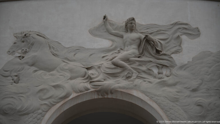White sculptural relief of a draped female figure with horses and billowing fabric above an arch on the Municipal Theatre.